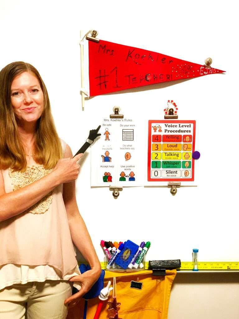A teacher at a white board pointing to her classroom rules for elementary school